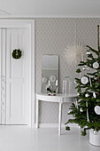 Christmas tree and console table with mirror against patterned wallpaper