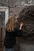 Woman attaching rustic wreath to house wall