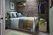 Simple metal bed with scatter cushions and throws against rustic board wall