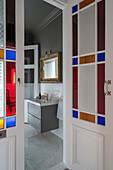 looking through the double doors with stained glass into a classic bathroom in grey and white