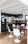 Open kitchen and dining area with antique wooden table and white classic chairs in loft flat