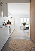 White kitchen and dining area, round natural jute carpet in the foreground