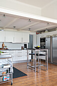 White fitted kitchen cabinets, stainless steel appliances, and breakfast bar, suspended from the ceiling