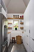 Narrow kitchen with white cupboards, shelves and fridge-freezer