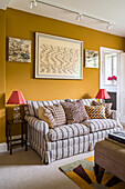 Sofa with striped cover and scatter cushions in sitting room with mustard-yellow wall