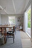 Esstisch aus Holz mit Stühlen vor Terrassentür, Sessel mit Fußschemel in Zimmerecke