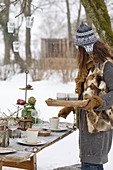 Frau verteilt Getränke am gedeckten Tisch im winterlichen Garten