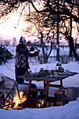Frau hängt Laternen an Baum über gedecktem Tisch in verschneitem Garten