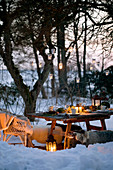 Hängende Laternen am Baum über gedecktem Tisch in verschneitem Garten
