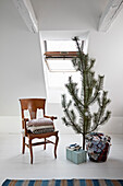Korb mit Geschenken unter dem Weihnachtbaum, daneben antiker Holzstuhl mit Decken