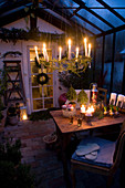 Hängender Kranz mit brennenden Kerzen über Esstisch in weihnachtlich dekoriertem Wintergarten