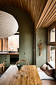 Dining table and bench by window in kitchen with green wood panelling