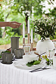 Gedeckter Tisch mit Blumenstrauß auf der Terrasse, Kerze wird angezündet
