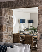 View through exposed granite doorway to dining room with denim fabric lamp shades