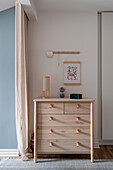 Chest of drawers made of light wood with leather handles, above it a hanging picture