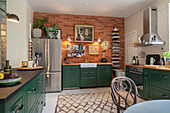 Base cabinets with green fronts in kitchen with exposed brick wall