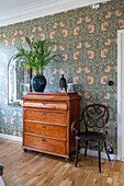 Antique chest of drawers with indoor palm tree in front of wallpapered wall