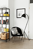 Black chair with scatter cushion between standard lamp and shelves in corner