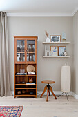 Beige living room with glass-fronted cabinet, swivel stool, floor lamp and shelves