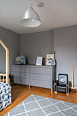 Grey 6 draw dresser in front of grey wall and small leather armchair in a children's room