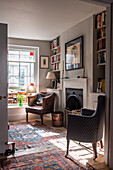 Fireplace flanked by bookshelves, upholstered armchair and vintage leather armchair in the background
