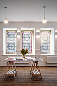 White table top on wooden trestles in front of stained glass windows