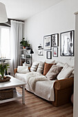 Rattan sofa with white blanket and scatter cushions below modern pictures on living room wall