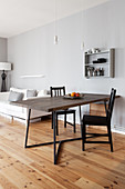 Dining table with dark wooden top and black chairs in open-plan interior