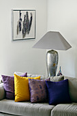 Tischlampe mit silbernem Lampenfuß hinter Sofa mit Kissen