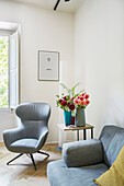Gray armchair, side table with flowers and sofa in the living room
