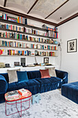 Blue velvet sofa with ottoman above bookshelf in living room