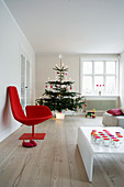 Roter Designerstuhl, weißer Couchtisch mit Windlichtern und Weihnachtsbaum im Wohnzimmer