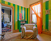Armchair in front of bookcase in room with green and yellow striped walls