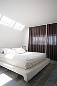 Double bed with white bed linen in bedroom with skylight
