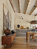 Sideboard, darüber großformatiges Bild in offener Küche mit sandfarbenen Wänden und Holzbalken