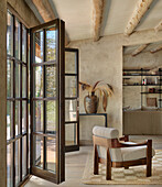 Sessel vor geöffneten Terrassentüren im Wohnraum mit sandfarbener Wand und Holzbalken