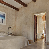 Doppelbett im Schlafzimmer mit sandfarbenen Wänden und Holzbalken