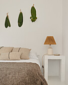 Bett und Nachttisch vor weißer Wand mit Kaktusblättern