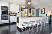 Island counter with concrete worktop and bar stools in open-plan kitchen