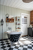 Freestanding bathtub in bathroom with wood paneling and black and white floor tiles
