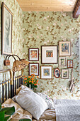 View over bed to gallery of photos on wall with floral wallpaper