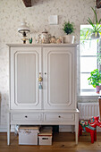 Tall cabinet in country-house style against patterned wallpaper
