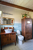Antique washstand, toilet and wooden cabinet in bathroom with light blue wall tiles