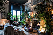Covered sofa in front of lit fire in London apartment filled with plants
