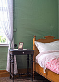 A wooden bed and a bedside table against a green wall in a bedroom