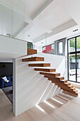 Floating wooden stairs on white wall in open plan living room