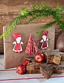 Wrapped gift with DIY paper Mrs Christmas decorations, wooden stars and apples in the foreground
