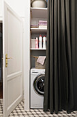 Waschmaschine und Regale mit Waschmitteln hinter Vorhang