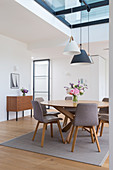A round dining table with grey chairs and a vintage chest of drawers in a loft apartment with a skylight
