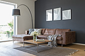 A brown leather couch, an arc lamp and a coffee table in front of a dark wall